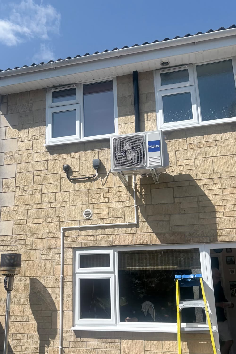 A Haier air conditioning condenser mounted on the outside wall of a house in Cheltenham
